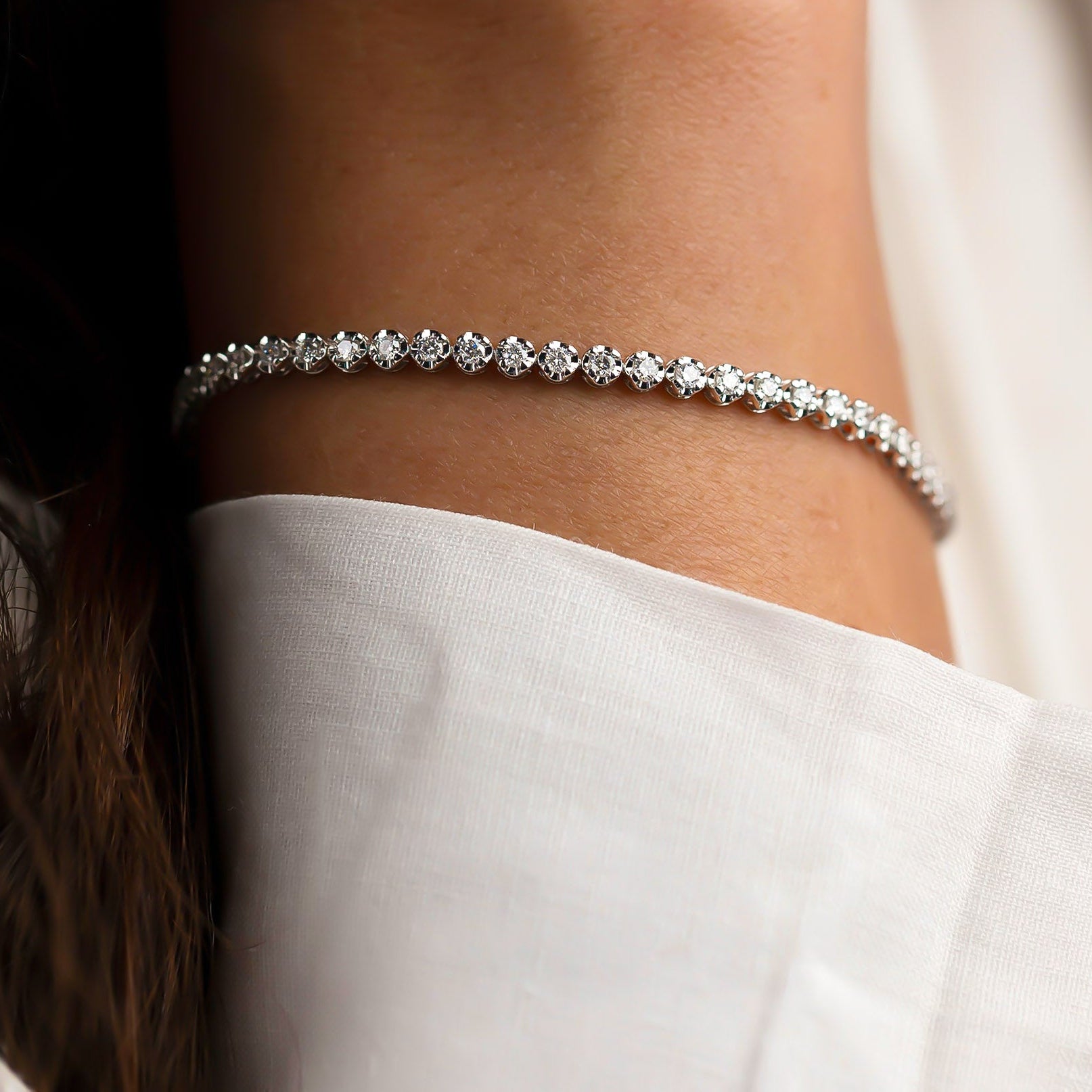 18 Karat Diamant Tennis Armband, getragen am Handgelenk vor hellem Stoff - elegantes und funkelndes Design.
