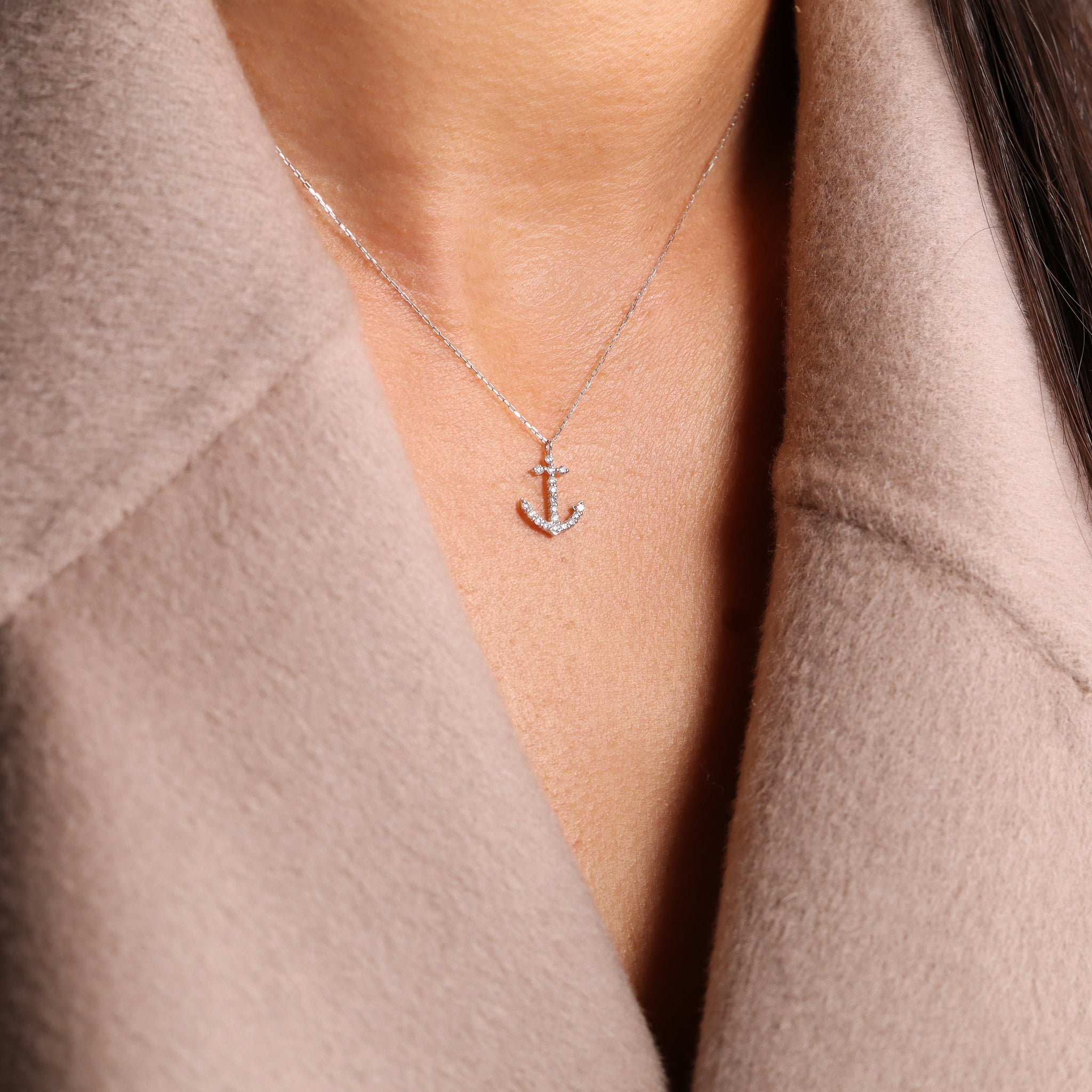 Damenhalskette aus 18k Weißgold mit diamantenbesetztem Anker-Anhänger, getragen über einem beigen Mantel.