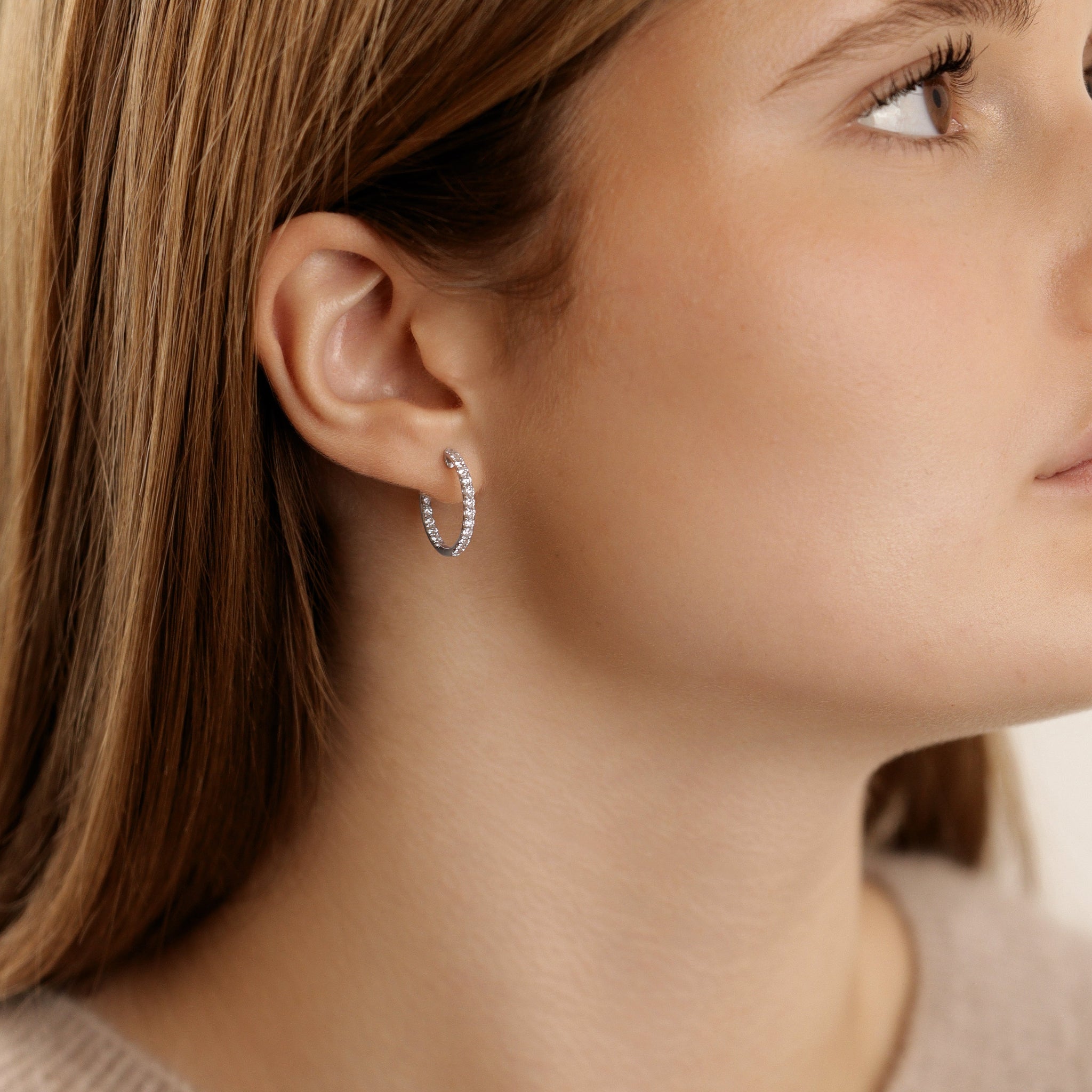 Seitliche Ansicht einer Frau, die 18-Karat-Weißgold-Creolen trägt, innen und außen mit Diamanten besetzt - funkelnder, eleganter Ohrschmuck.