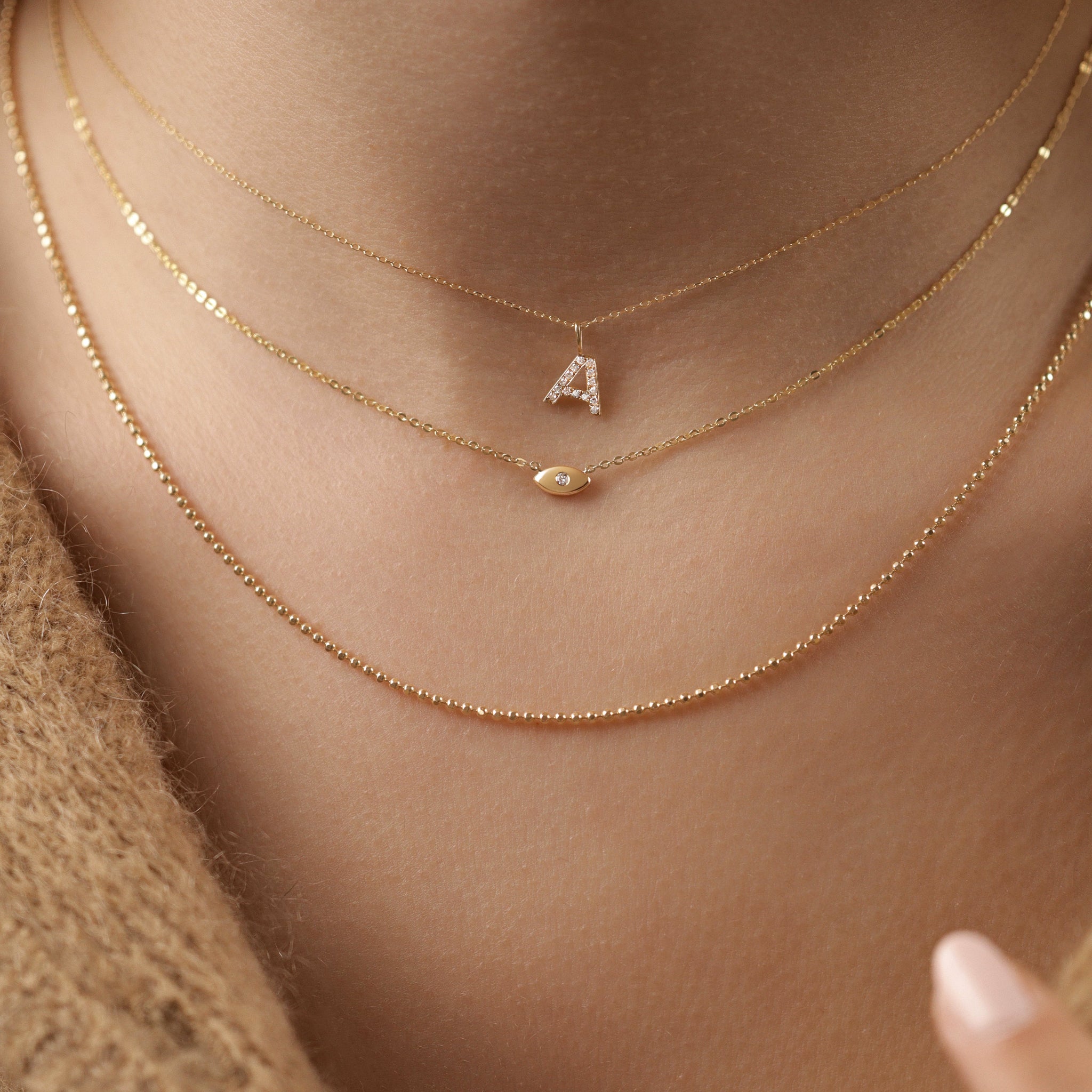Lucky Eye Halskette aus 18k Gold, getragen im Layering-Loo mit Buchstabenanhänger - zarte Schutzsymbol-Kette für Damen.